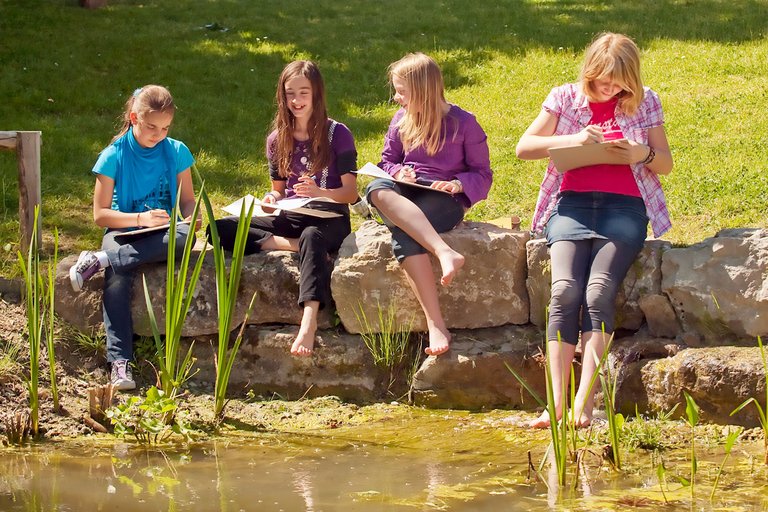 Studenti sede na zidu na ivici jezerceta i farbaju.