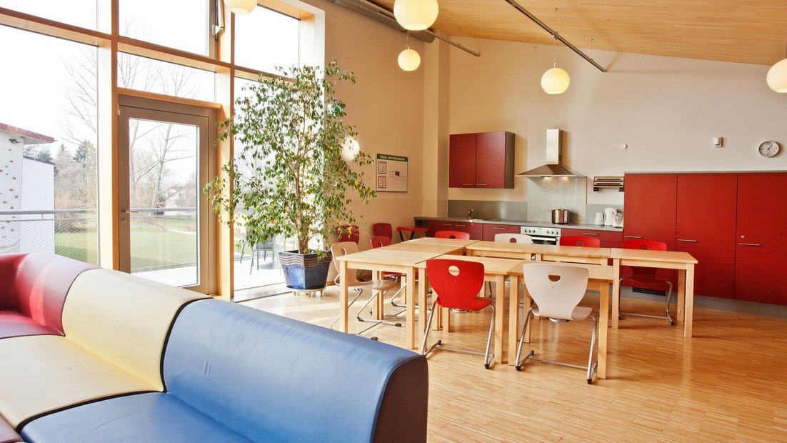 Gornji zajednički prostor u Wiesenhausu sa balkonom: sa crvenom čajnom kuhinjom, grupom trpezarijskih stolova i prostorom za sedenje u prvom planu