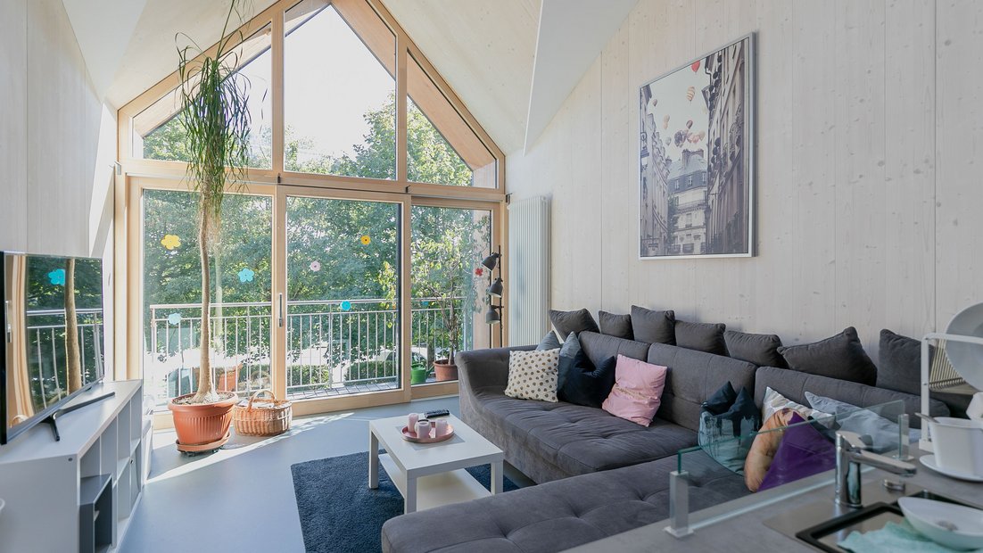 Udoban zajednički prostor na spratu sa velikim uglom sive sofe i pogledom kroz veliki balkonski prozor